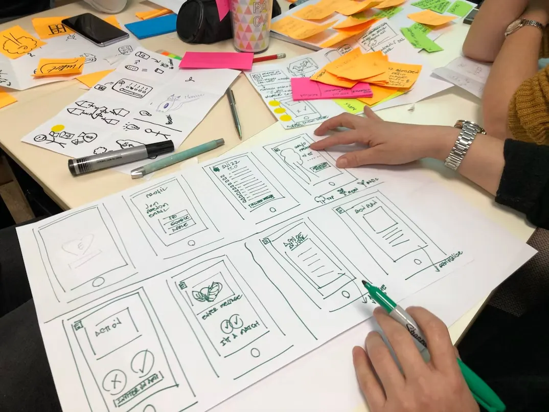 Two people sketching wireframes with sticky notes on a table
