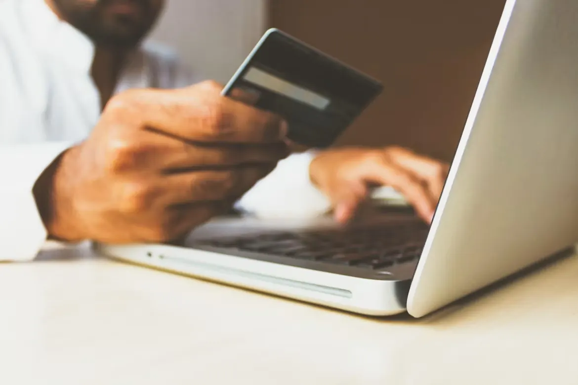 A person holding a payment card while shopping on a laptop