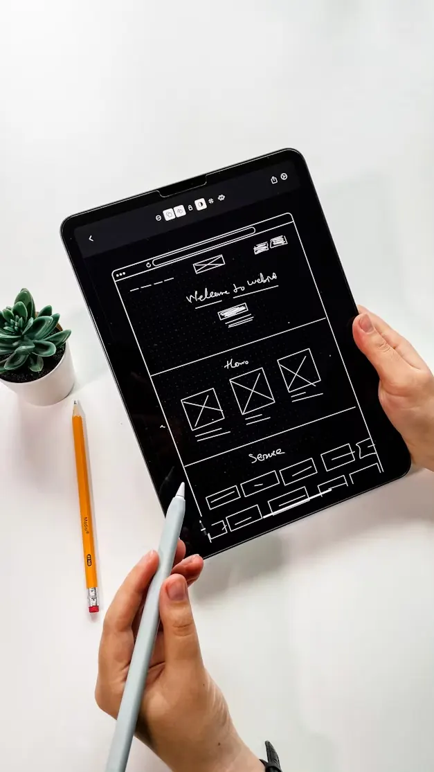 A hand sketching a website wireframe on a tablet