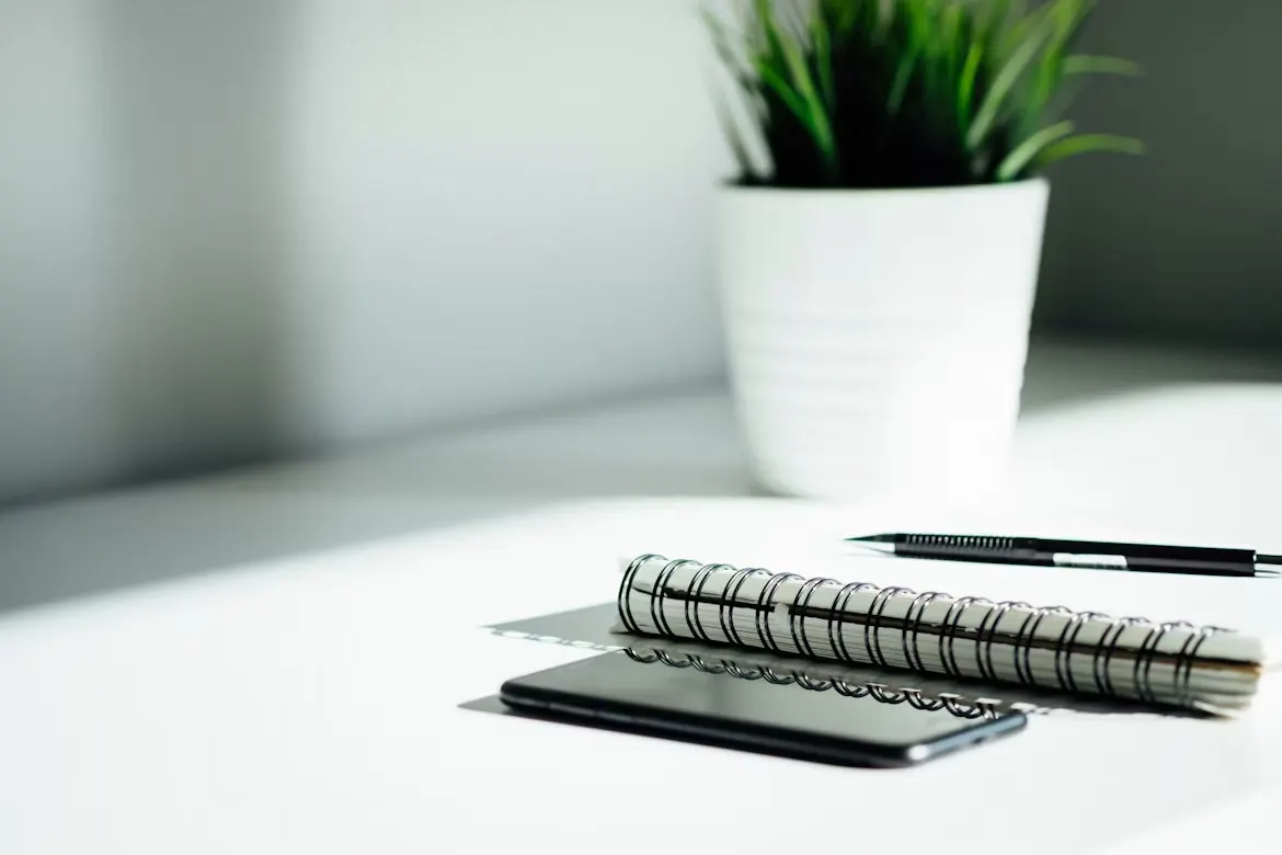 A notebook, pen and phone on a bright desk